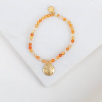 Bracelet with orange beads and gold sand dollar charm on a white background