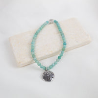 Turquoise-color amazonite beaded bracelet with a silver sand dollar pendant on a white background