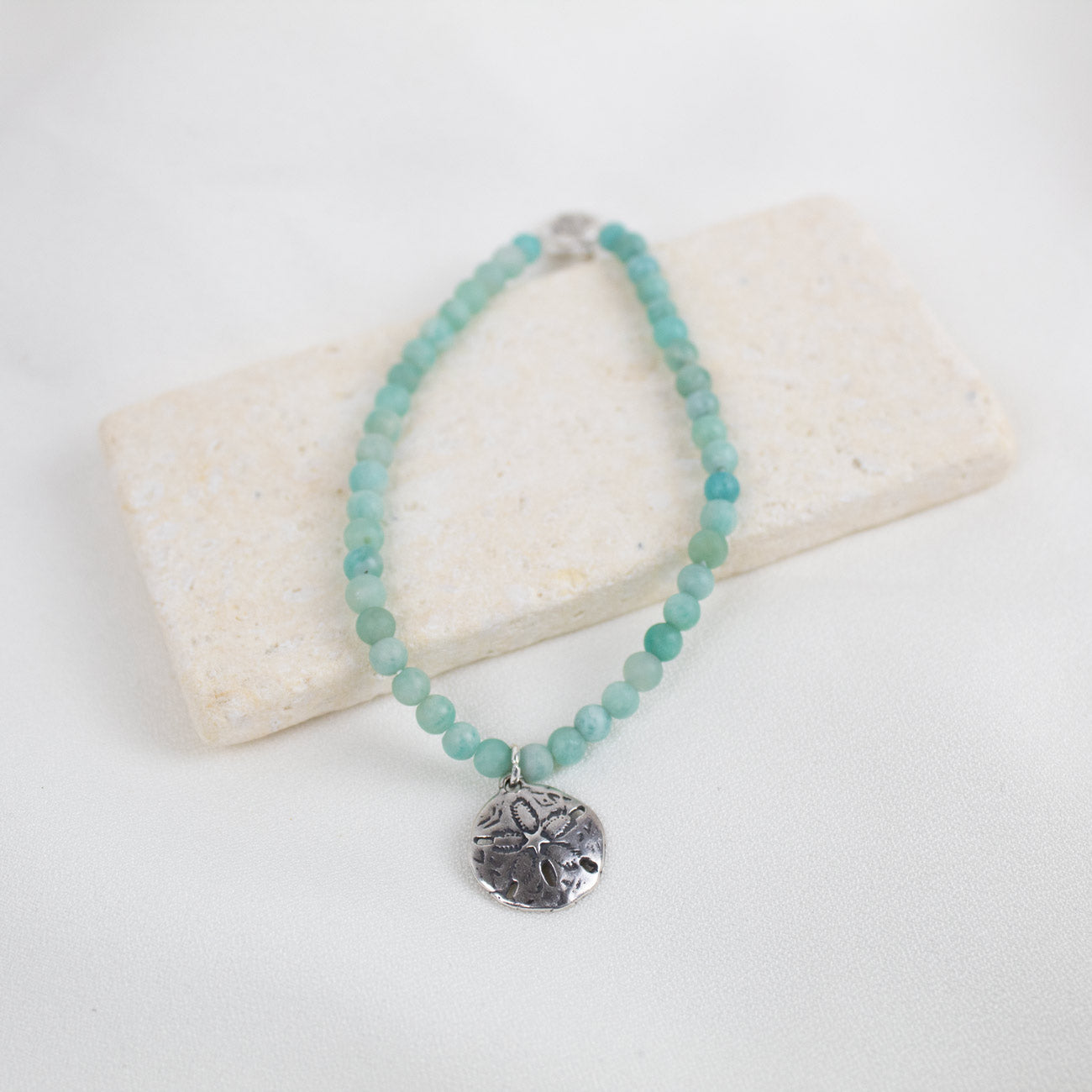 Turquoise-color amazonite beaded bracelet with a silver sand dollar pendant on a white background