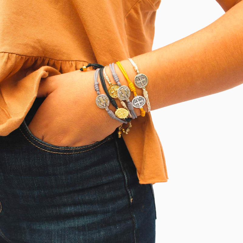 Young person wearing stack of neutral color woven corded Serenity Blessing Bracelets with the Benedictine Medal of protection