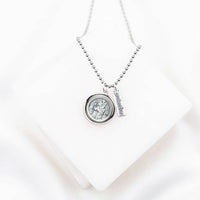 A silver necklace with a round St. Christopher/Archangel Michael medallion pendant and a vertical 'protection' charm, displayed on a white geometric block against a white background.
