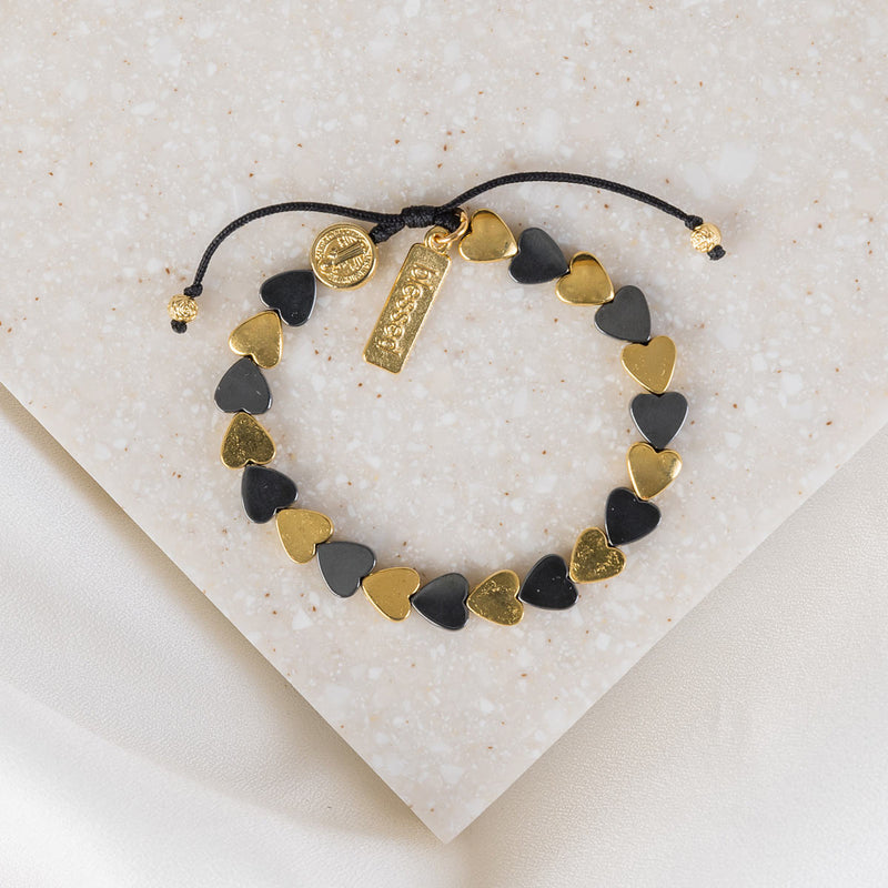 gold and black hematite hearts in alternating pattern. witha st. benedictin medal and a blessed charm tag on black slip knot cording