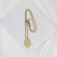 Gold necklace with a pendant on a white textured surface