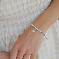 Close-up of a wrist wearing a bracelet with a small St. Ignatius of Loyola saint charm, against a neutral background.