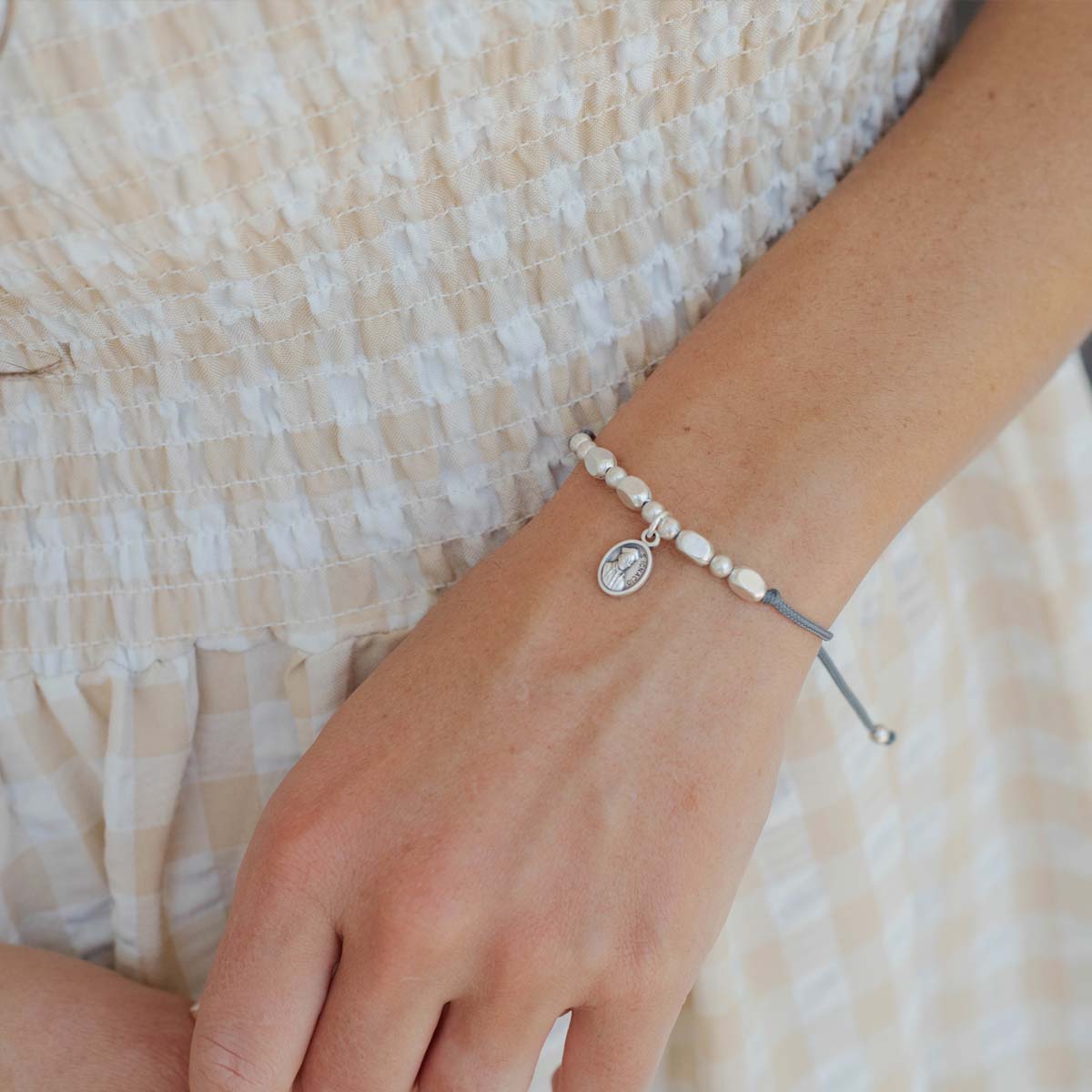 Close-up of a wrist wearing a bracelet with a small St. Ignatius of Loyola saint charm, against a neutral background.
