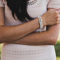 Person wearing a light pink dress with lace details and a bracelet on a blurred natural background