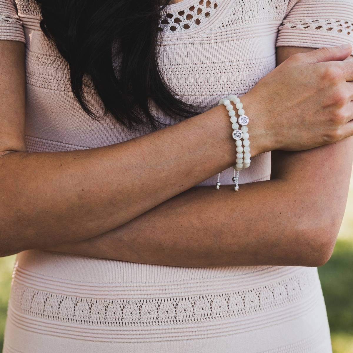 Person wearing a light pink dress with lace details and a bracelet on a blurred natural background
