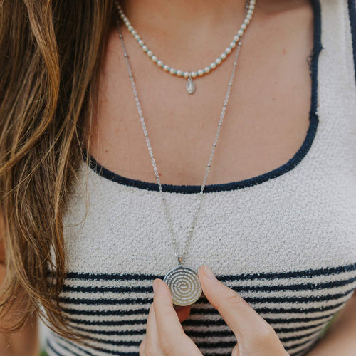 Person wearing a striped top with layered necklaces, holding a spiral pendant.