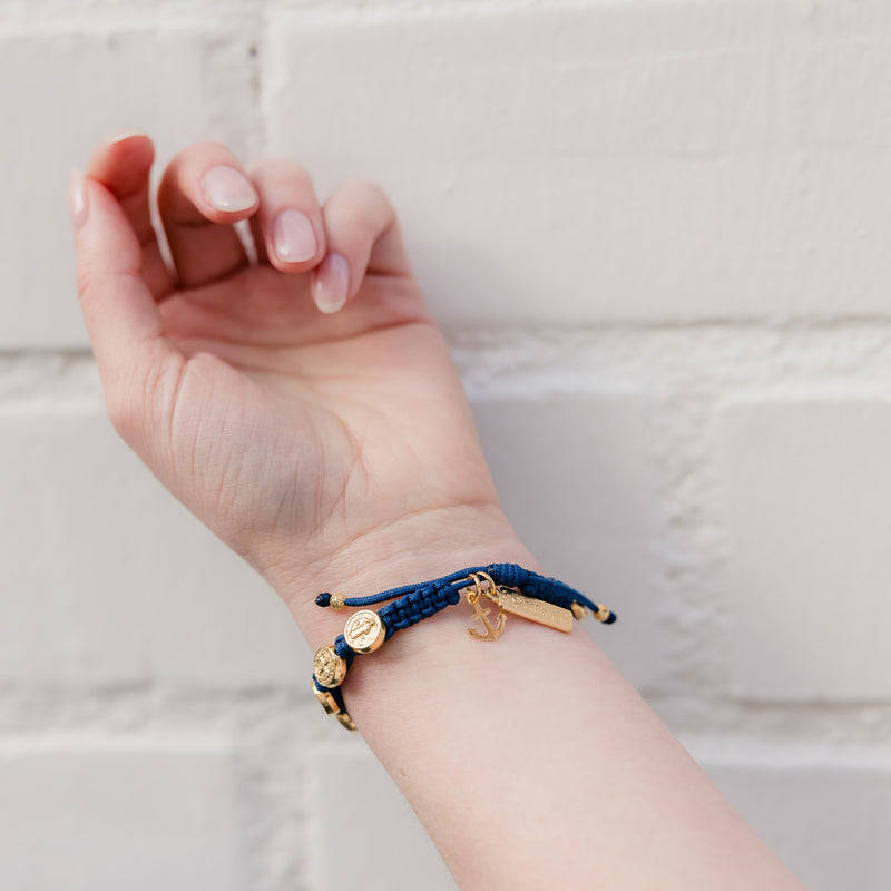close up of wrist with a blue and gold handwoven benedictine blessing bracelet with an anchor charm in gold tone
