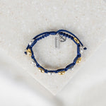 overhead shot of blue handwoven bracelet with alternating gold and silver benedictine medals and a silver blessed charm and silver anchor charm
