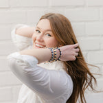 woman smiling wearing a stack of all three trust the journey silver and gold st. benedict medal handwoven bracelets