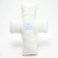 A plush, white weighted pillow in the shape of a cross with a label that reads 'Huggable Blessings'.