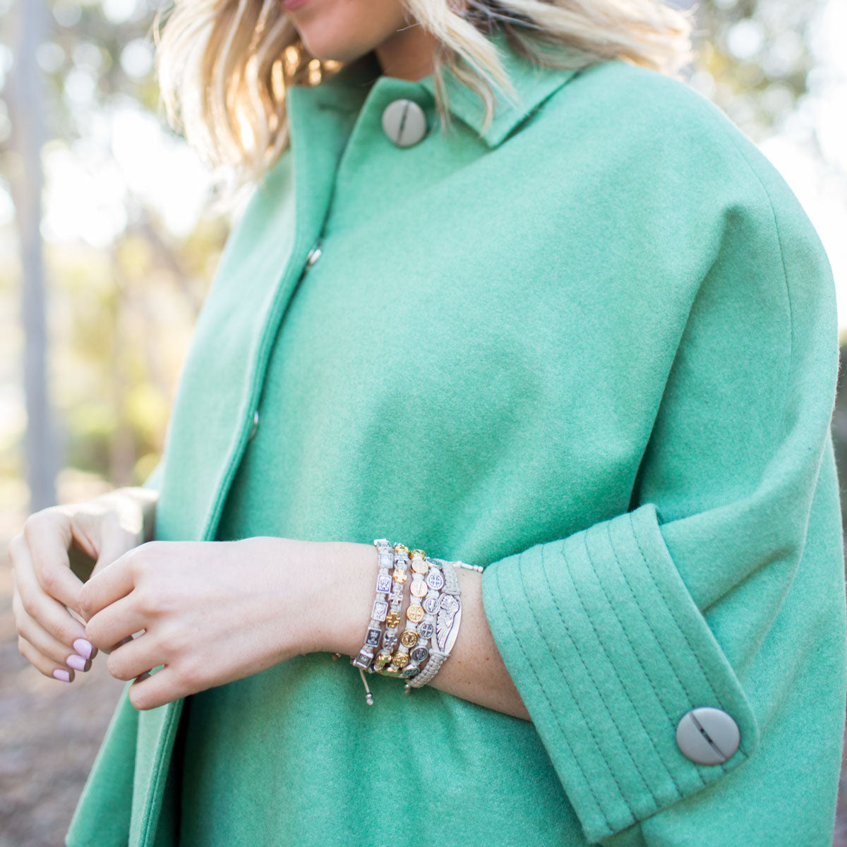 woman in green coat wearing a wing of protection bracelet and other my saint my hero handwoven blessing bracelets