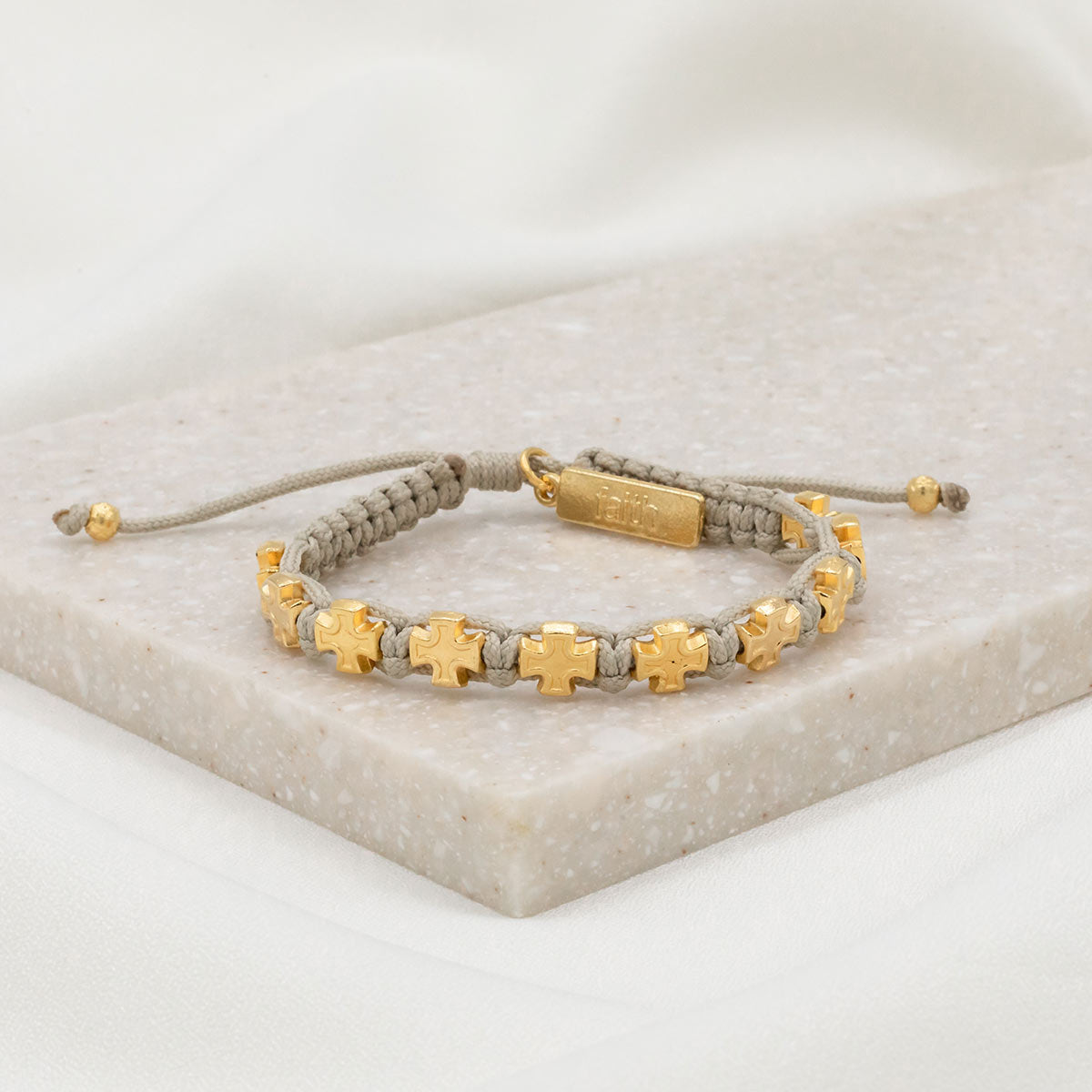 tan handwoven knotted cording slipknot bracelet with gold tone cross medals and a gold tone faith charm tag