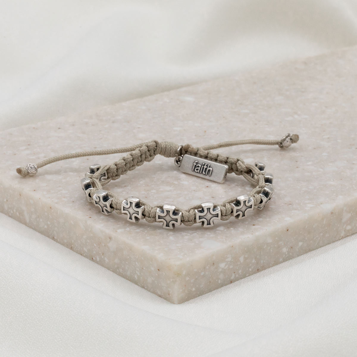 ten cross medals in silver tone on tan bracelet cording with charm tag with the word faith at the slip knot closure