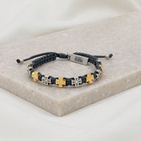 slate woven bracelet with alternating silver and gold tone medals and a silver charm tag at the slip knot closure with the word faith