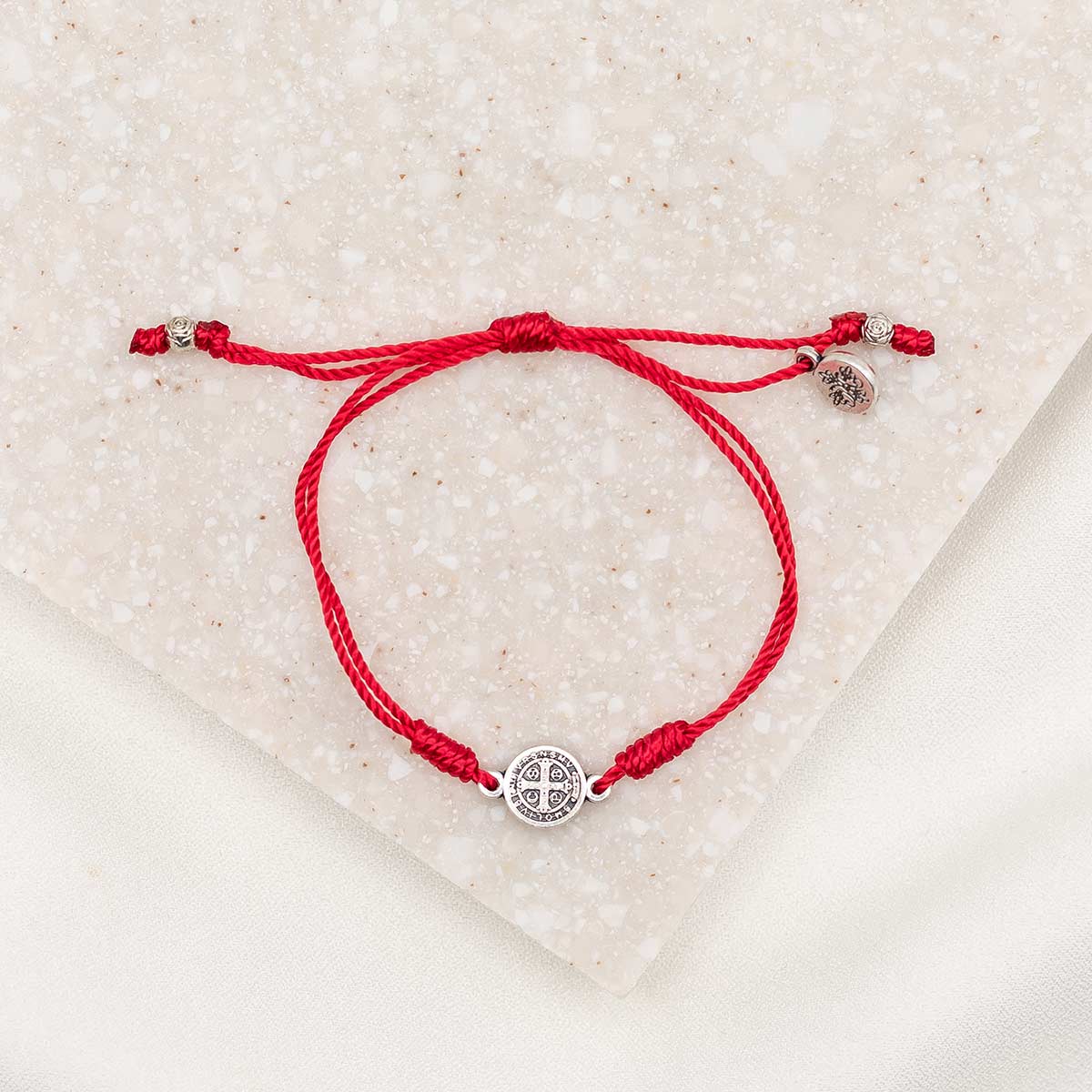silver-tone St. Benedict medal on red bracelet cording with a slipknot closure