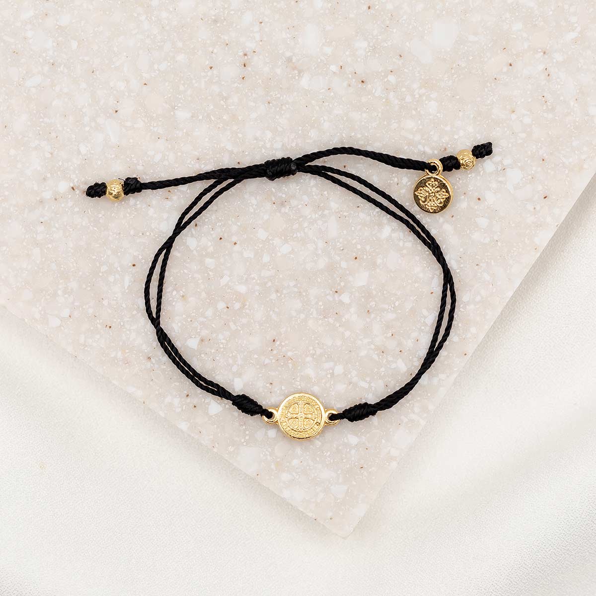gold-tone St. Benedict medal on black bracelet cording with a slipknot closure