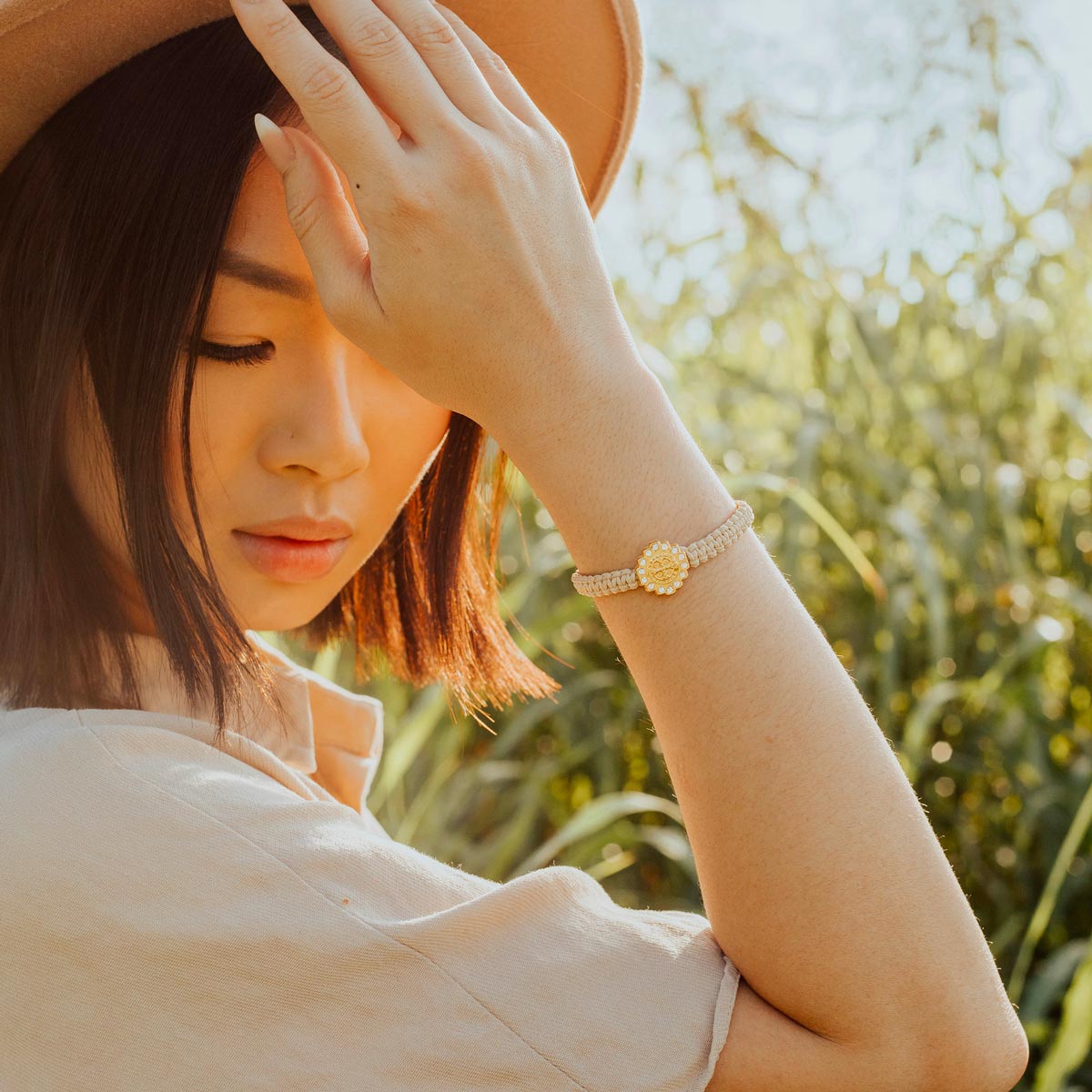 Woman in field wearing a tan wool hat and a cream and gold tone St. Benedict Brilliance Blessing Bracelet