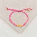 overhead photo of pink slip knot bracelet with gold medals and the word hope on white background