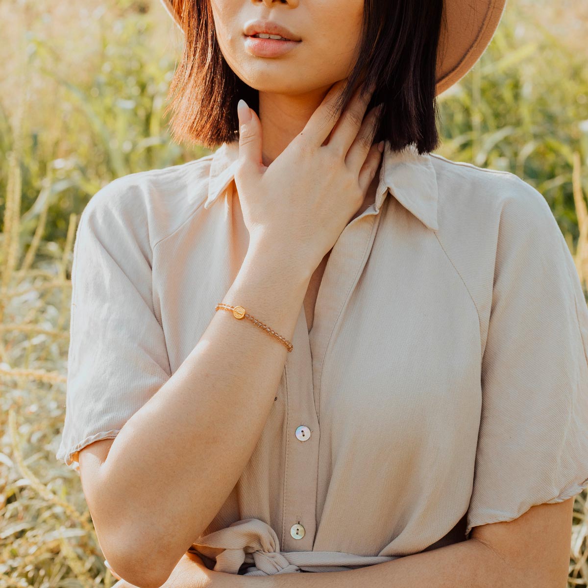 Young woman in field wearing a Shine Bright Crystal Blessing Bracelets in gold crystal and gold tone St. Benedict Medal