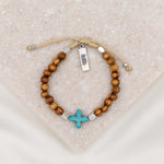 Grounded in Faith Olive Bead Bracelet with blue dyed cross, silver tone faith charm tag, on tan bracelet cording