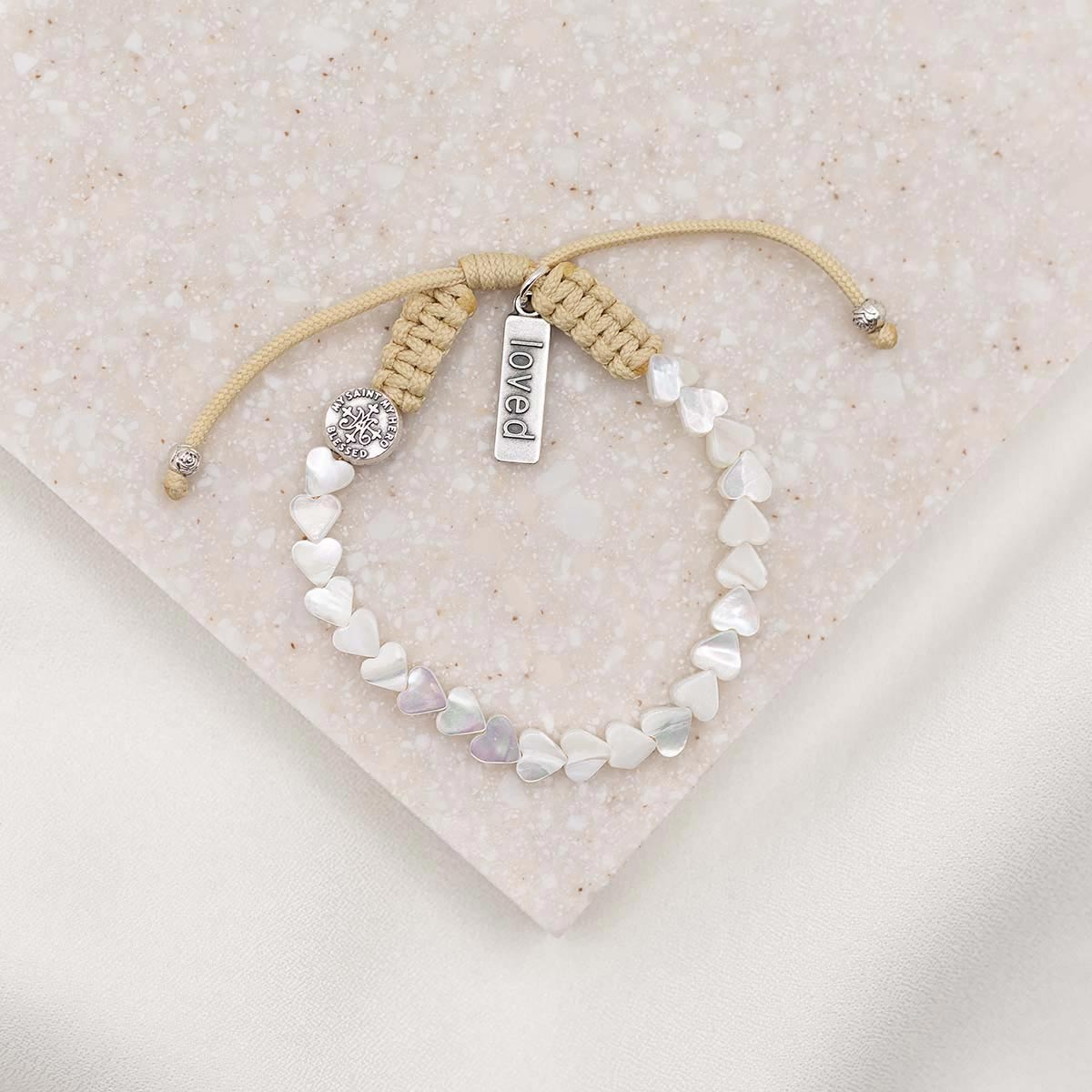 mother of pearl heart bracelet on tan woven cording with silver loved charm tag and silver blessed medal bead