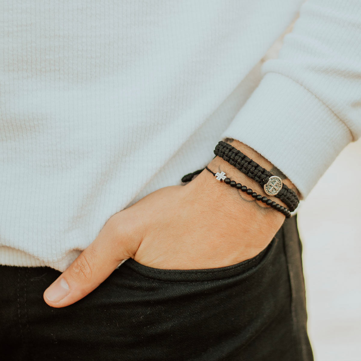 Close up of man's wrist wearing 33 black onyx beaded and silver tone cross Jesus  Prayer Bracelet with a Black woven cording and St. Benedict Men's One Blessing Bracelet