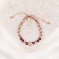An adjustable bracelet with pink and purple crystals and a gold-tone St. Amos medal, displayed on a white surface.