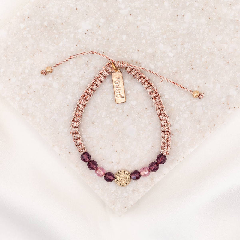An adjustable bracelet with pink and purple crystals and a gold-tone St. Amos medal, displayed on a white surface.