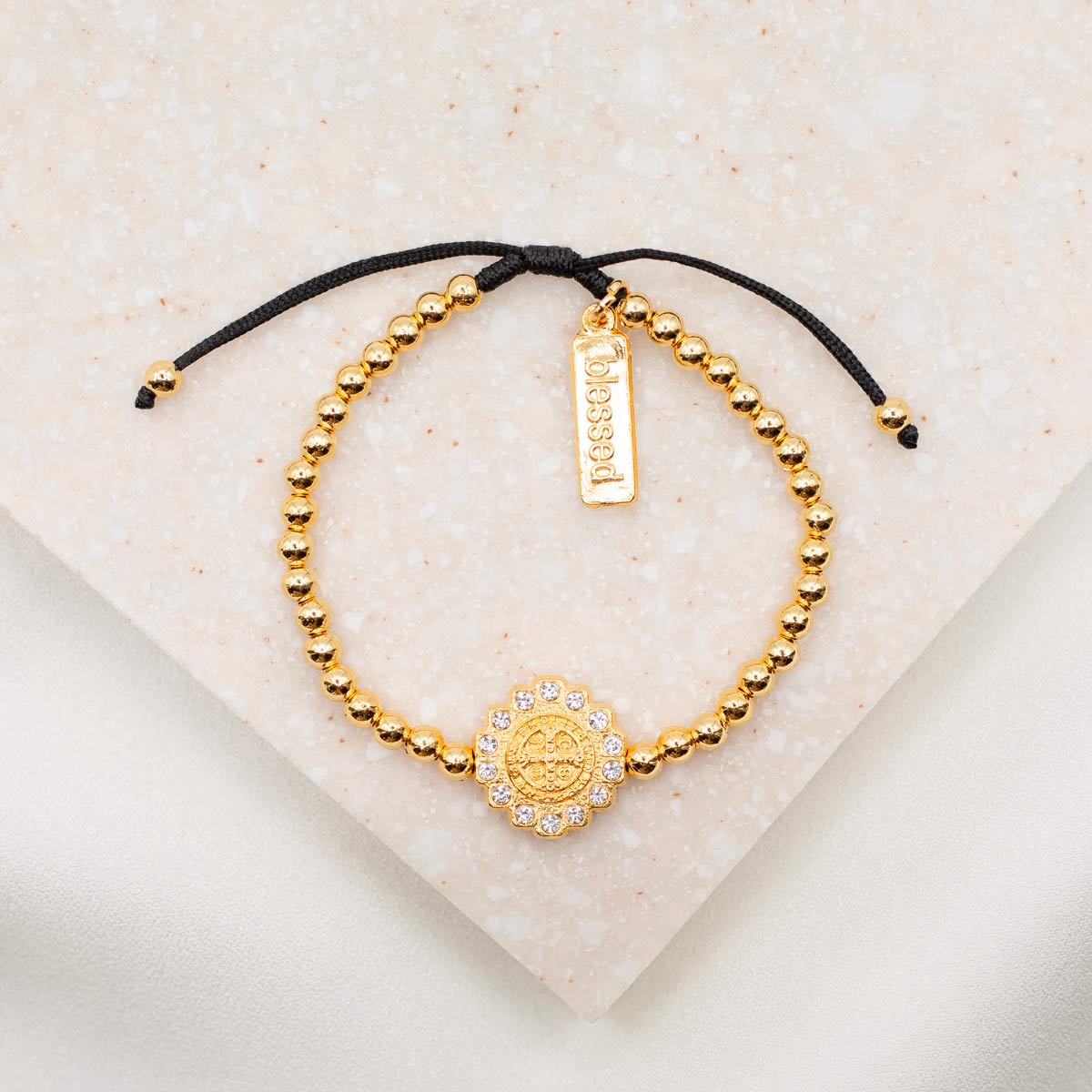 Mantra of Beauty & Brilliance Bracelet gold tone Benedictine Medal surrounded by crystals with gold tone beads on black woven slip know bracelet cording