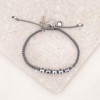 over head shot of Little Words Project and My Saint My Hero Faith Bracelet showing cross and logo charms
