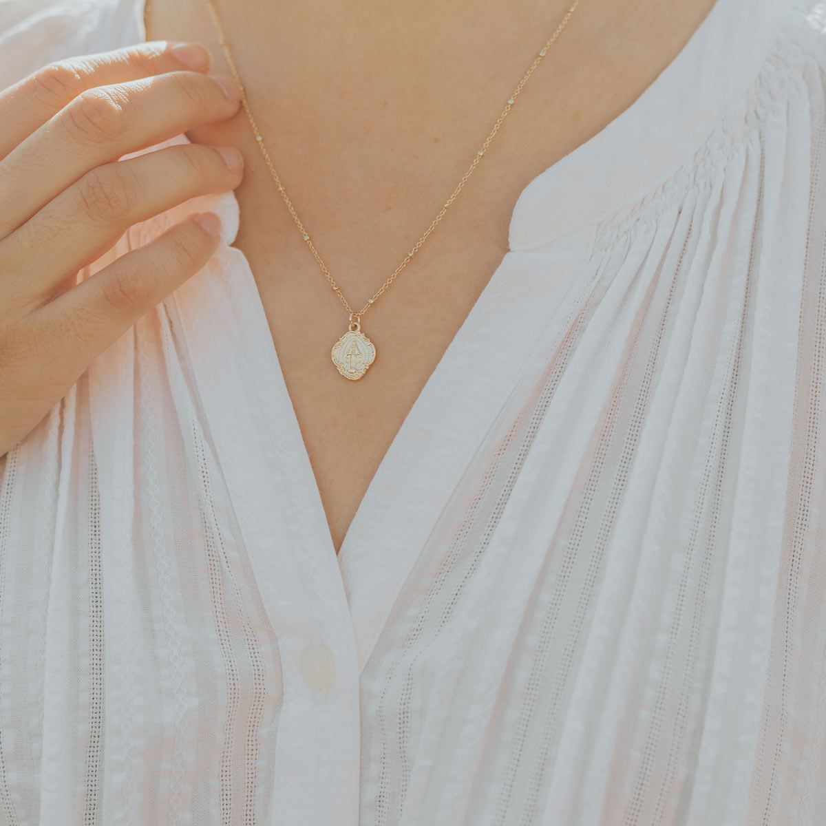Gold Mary Medal on a petite gold dipped station chain worn by a women in a white blouse