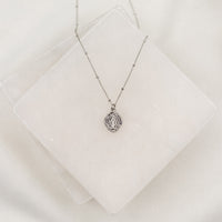 A delicate necklace featuring a Miraculous Mary saint medal on a chain, displayed against a white background.