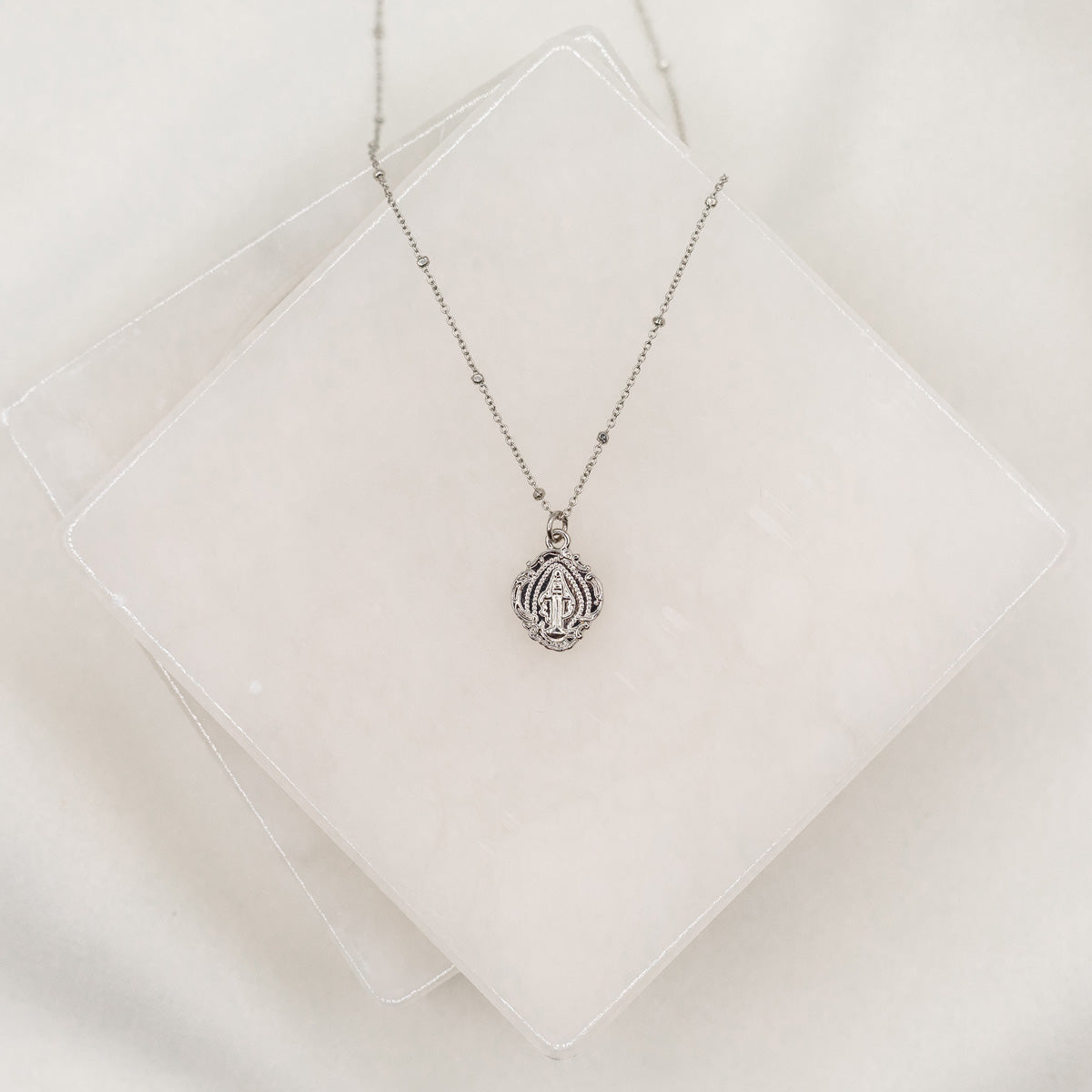 A delicate necklace featuring a Miraculous Mary saint medal on a chain, displayed against a white background.