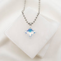 A silver-colored cross necklace with a large, clear, square-shaped crystal pendant, displayed against a white background.