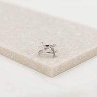 A sterling silver cross ring placed on a beige surface, with the ring's band adjusted to a size that fits most fingers.