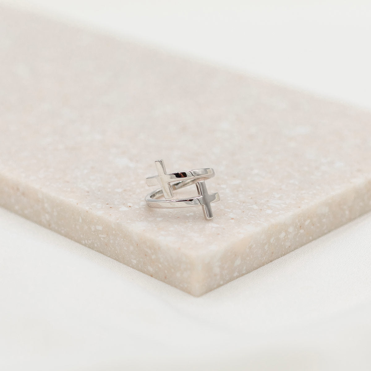 A sterling silver cross ring placed on a beige surface, with the ring's band adjusted to a size that fits most fingers.