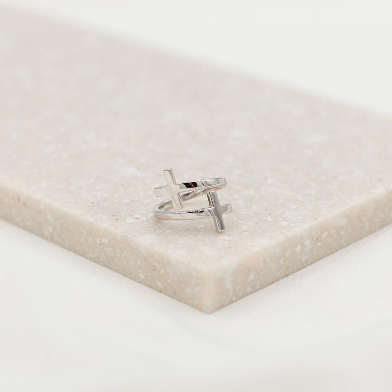 A sterling silver cross ring placed on a beige surface, with the ring's band adjusted to a size that fits most fingers.