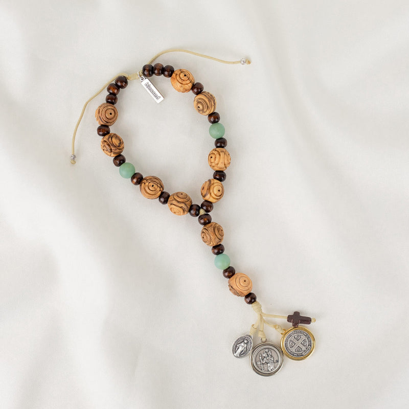 A door hanger made of hand-carved olive wood, featuring a two-tone Benedictine medal, a howlite cross, and silver-tone Miraculous Mary and Archangel Michael medals.
