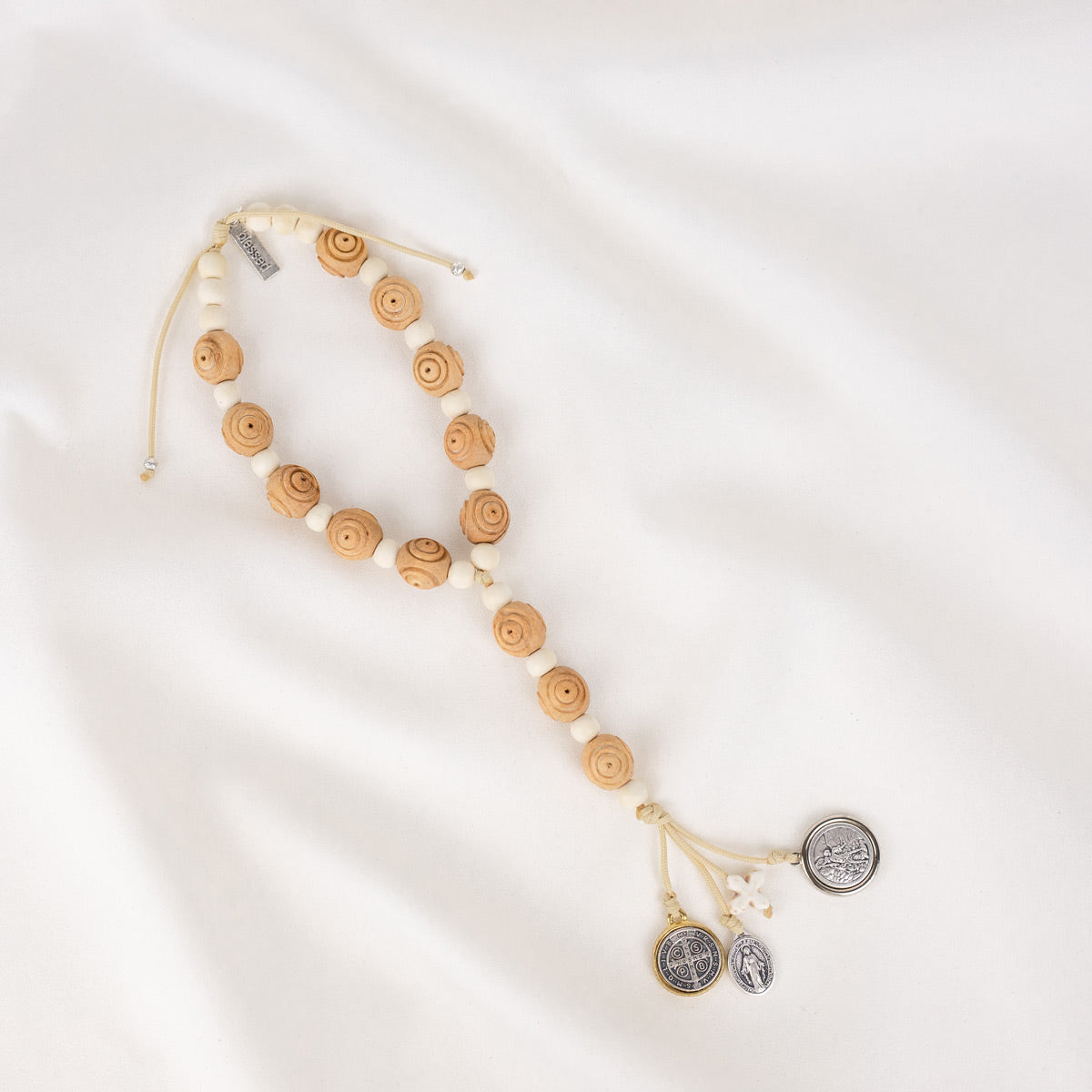 A door hanger made of hand-carved olive wood, featuring a two-tone Benedictine medal, a howlite cross, and silver-tone Miraculous Mary and Archangel Michael medals.