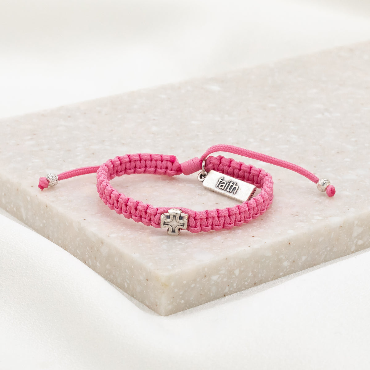 pink cording woven slip knot bracelet with silver tone medal and silver tone faith tag