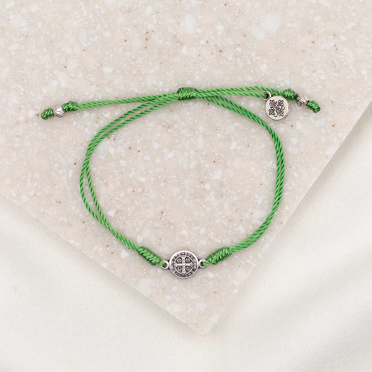 A green bracelet with a silver-tone Benedictine medal and a logo charm, displayed on a white surface.