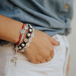 God Bless America Blessing Bracelet with Red and Silver My Saint My Hero Blessing Bracelets on a wrist with the hand in white denim pants pocket