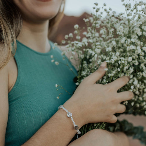 Close up of young woman holding baby's breathe bouquet and wearing a silver/clear crystal New Beginnings Bracelet