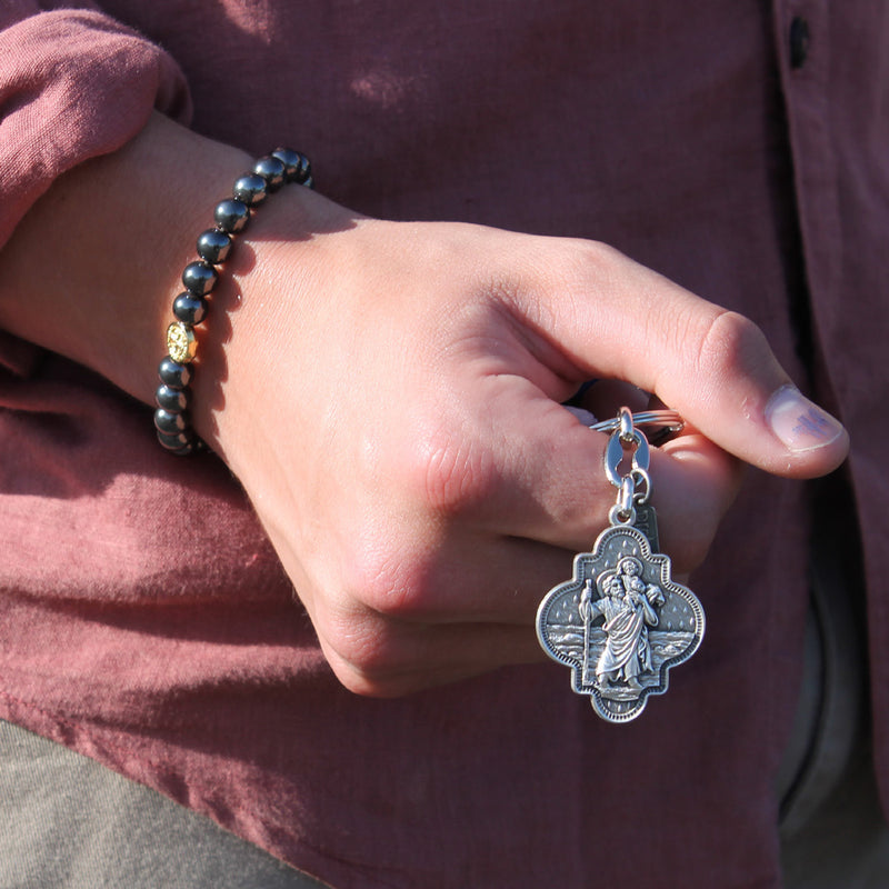 person holding Saint Christopher Travel Protection Key Ring and wearing a Strength Hematite Gemstone Saint Benedict Blessing Bracelet