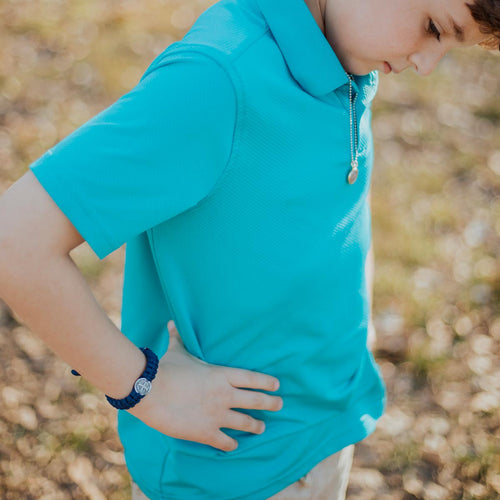 Boy in turquoise shirt with his hands on his hips wearing a navy One Blessing for Kids and Teens Bracelet