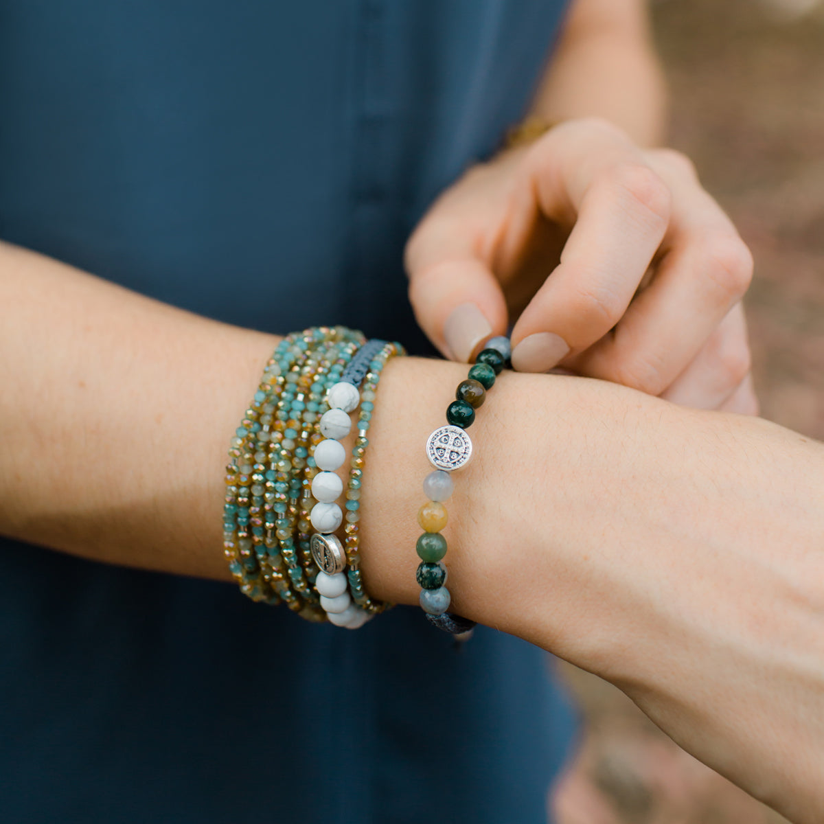 Wake Up and Pray Blessing Bracelets with hematite and mixed agate gemstones and saint benedict medals worn iwth a green and amber beaded morse code prayer rope around a woman's wrist