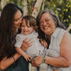 Caitlin Stamos and her mother holding her son and smiling with trees in the background, the grandmother is wearing My Saint My Hero Silver Crystal St Amos A Grandmothers Love Blessing Bracelets