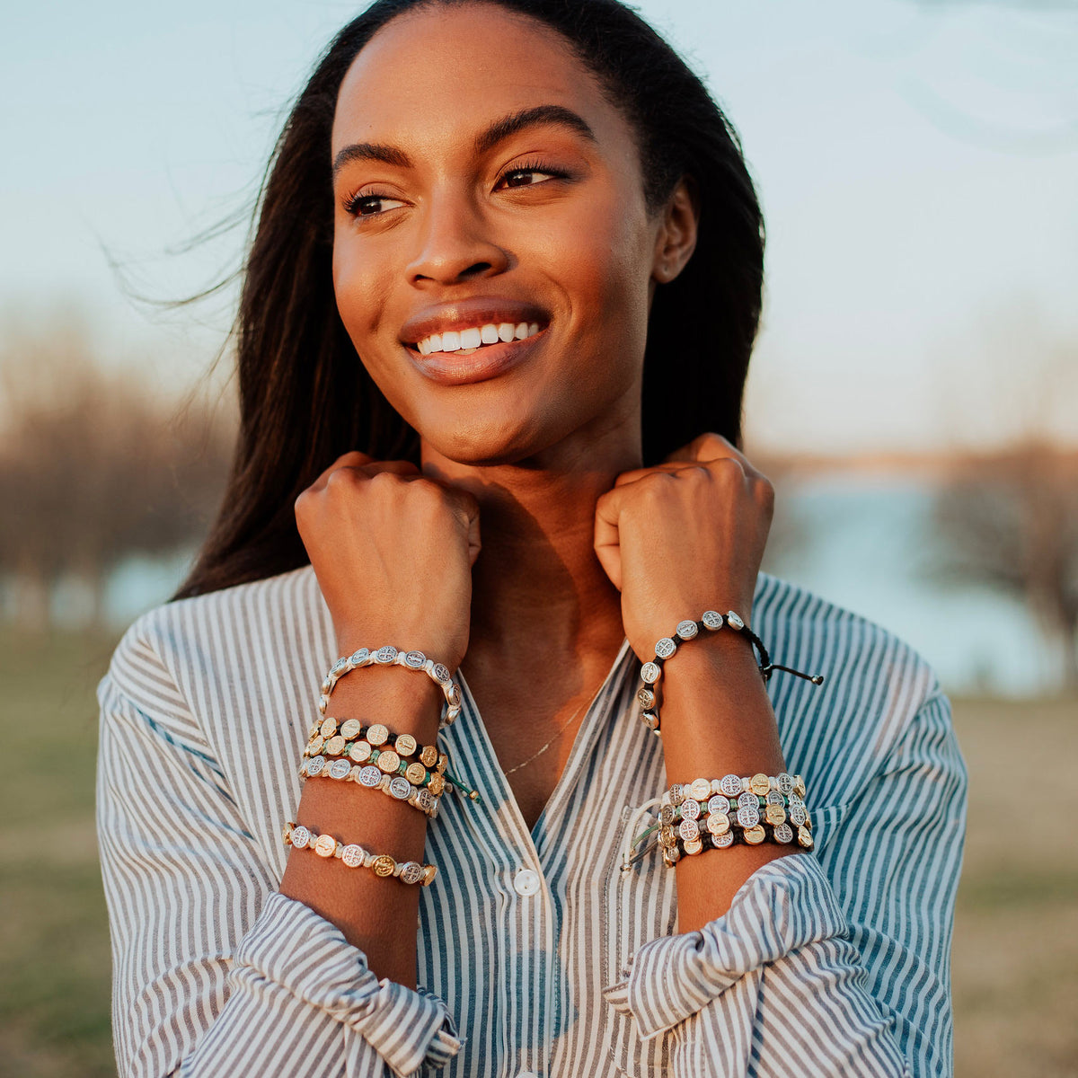Woman in striped shirt wearing stack of Benedictine Blessing Bracelets in a variety of colors